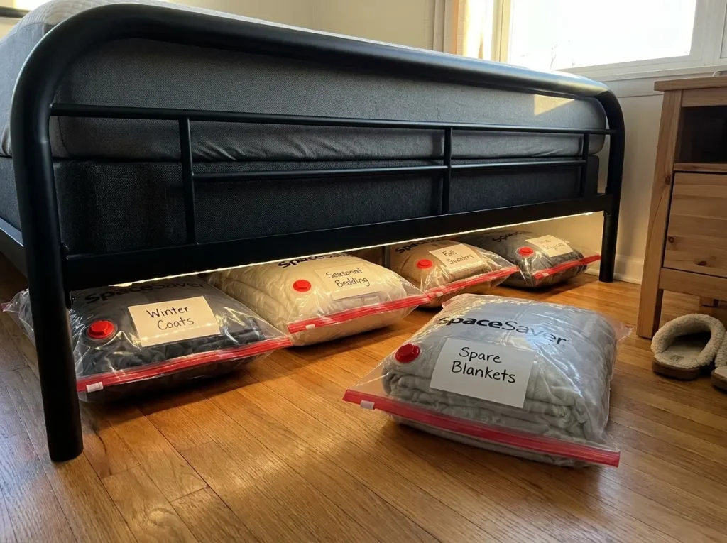 SpaceSaver vacuum storage bags with red valves stored flat and labeled under metal bed frame with easy slide-out access