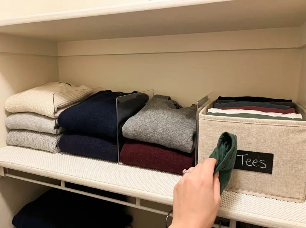 Why Your Closet Shelf Piles Keep Falling Over 5 Organized closet shelf with folded sweater stacks separated by acrylic dividers and fabric bin of file-folded shirts