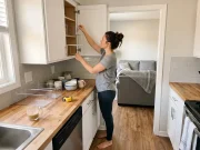 How to Organize Kitchen Cabinets That Stay Neat Woman organizing kitchen cabinets with bins and shelf risers on the counter