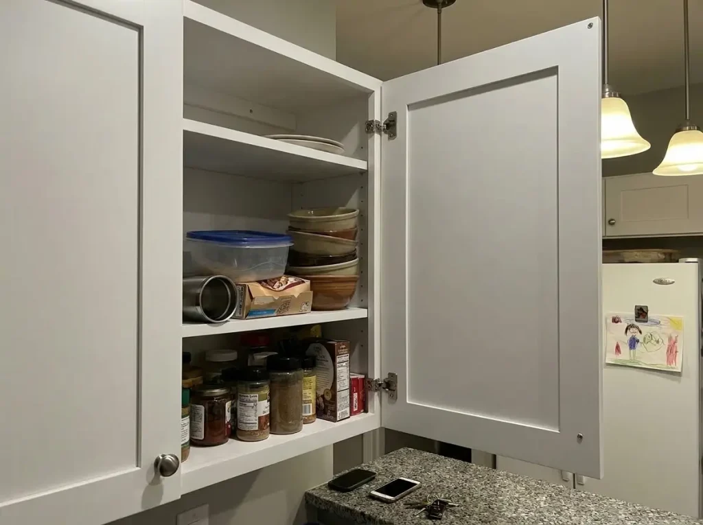 Messy kitchen cabinet with stacked bowls and items falling forward when opened