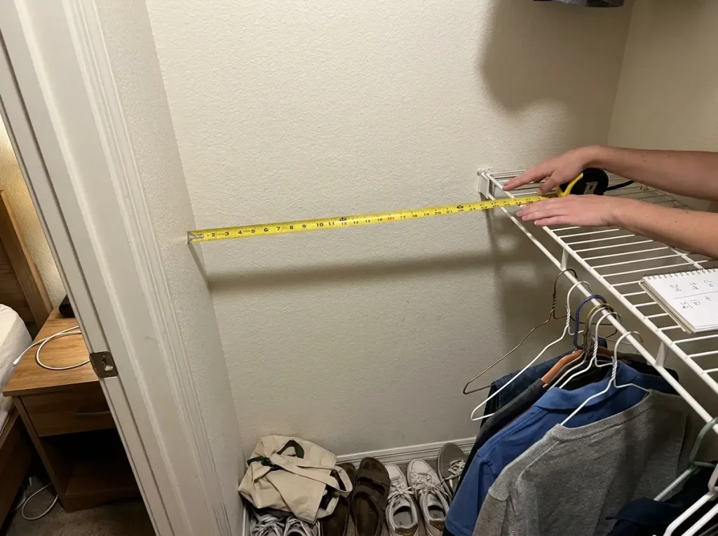 Hands holding a tape measure against a reach-in closet shelf showing depth measurement