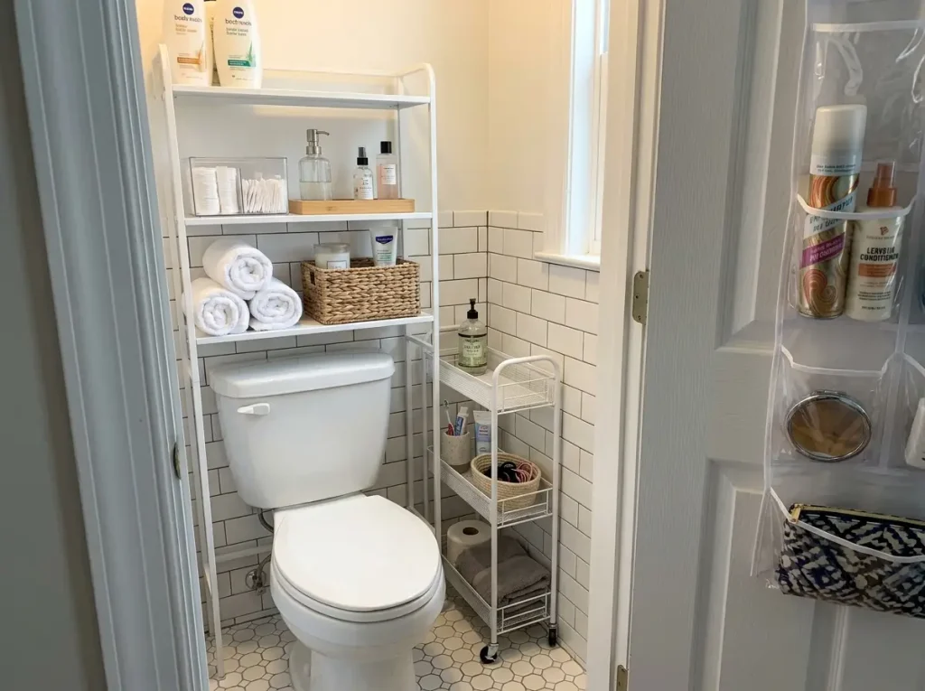 Organized bathroom toilet zone with white over-toilet shelf unit, slim rolling cart in gap, and 5-tier over-door organizer visible
