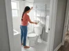 I Tested 6 Over-Toilet Shelves and This One Held Up Woman measuring over-toilet storage shelf in small white bathroom