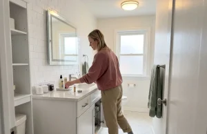 11 Small Bathroom Storage Ideas That Fit Real Spaces Woman organizing a small bathroom counter with labeled bins and a tray system in a compact rental bathroom