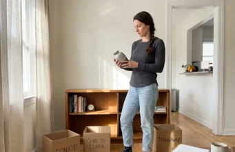 Afraid of Swedish Death Cleaning? Here’s What It Really Is Woman sorting belongings into labeled donation boxes during Swedish death cleaning in a living room