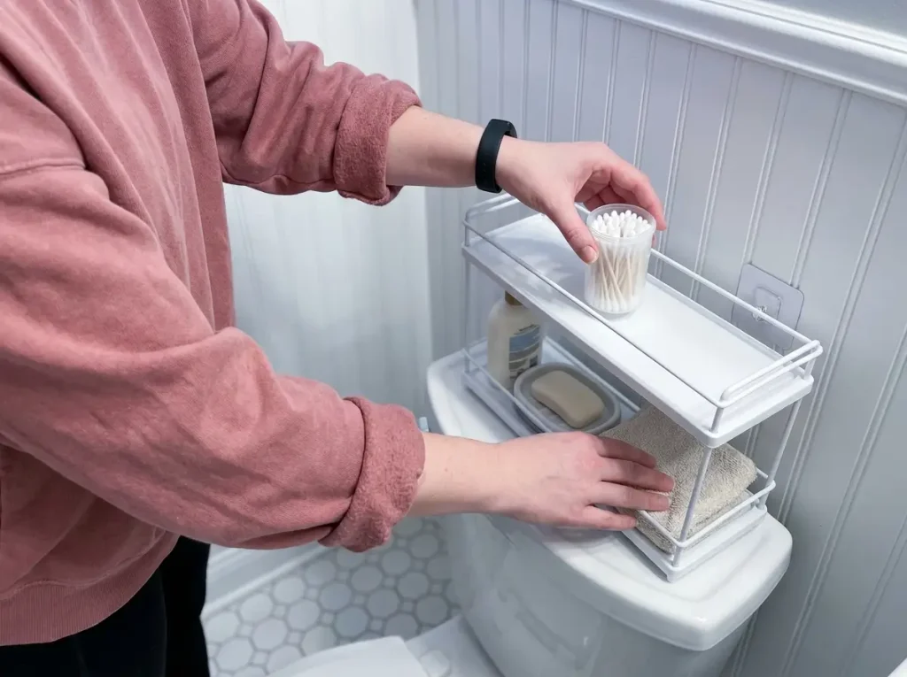 Hand placing small organizer on toilet tank caddy in compact bathroom