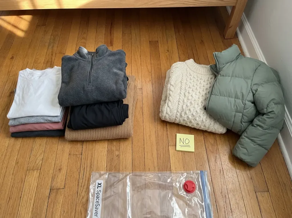 Clothes sorted on bedroom floor showing cotton and fleece items safe for vacuum sealing beside wool sweater and down jacket to avoid