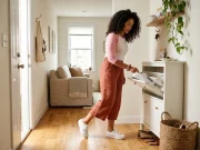 9 Entryway Shoe Storage Ideas That Stop the Pile Woman setting shoes into a slim entryway cabinet by a tight front door with a basket nearby