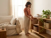 Minimalist Home Organization Without the Bin Trap Woman setting up minimalist home organization on open shelving with a few woven baskets in a bright living space