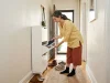 Shoe Storage Ideas for Small Spaces, Room by Room German American woman sorting shoes into a slim entryway cabinet in a small apartment hallway