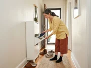 Shoe Storage Ideas for Small Spaces, Room by Room German American woman sorting shoes into a slim entryway cabinet in a small apartment hallway