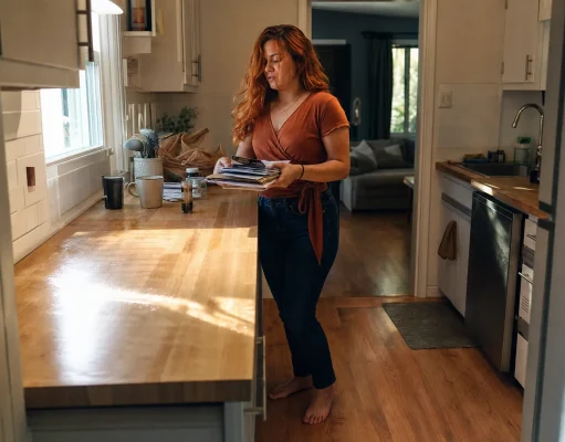 How to Declutter Kitchen Counters for Good Woman mid-way through decluttering a kitchen counter, clearing items into a sorting pile
