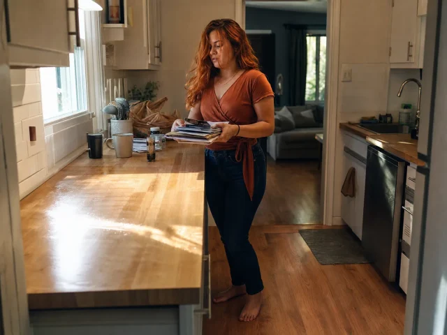 0-how-to-declutter-kitchen-counters-hero Woman mid-way through decluttering a kitchen counter, clearing items into a sorting pile