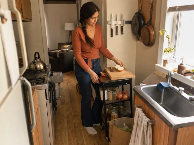 Woman prepping in a tiny kitchen with no counter space, using a rolling cart top as a surface
