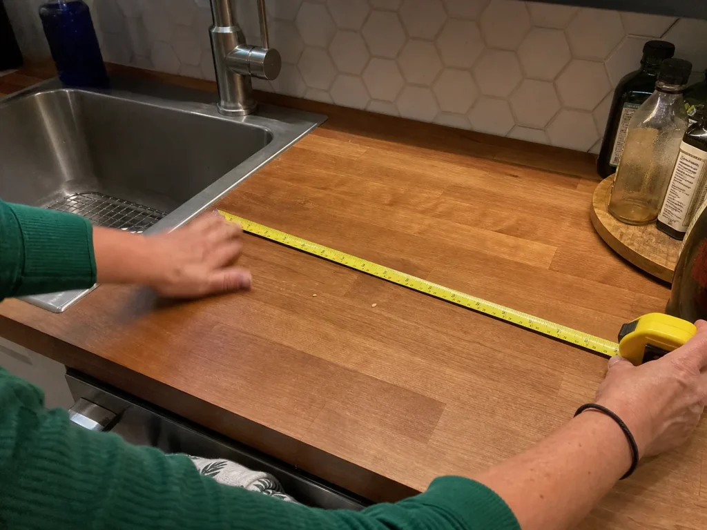 Hands measuring the clear prep zone on a kitchen counter with a tape measure before buying