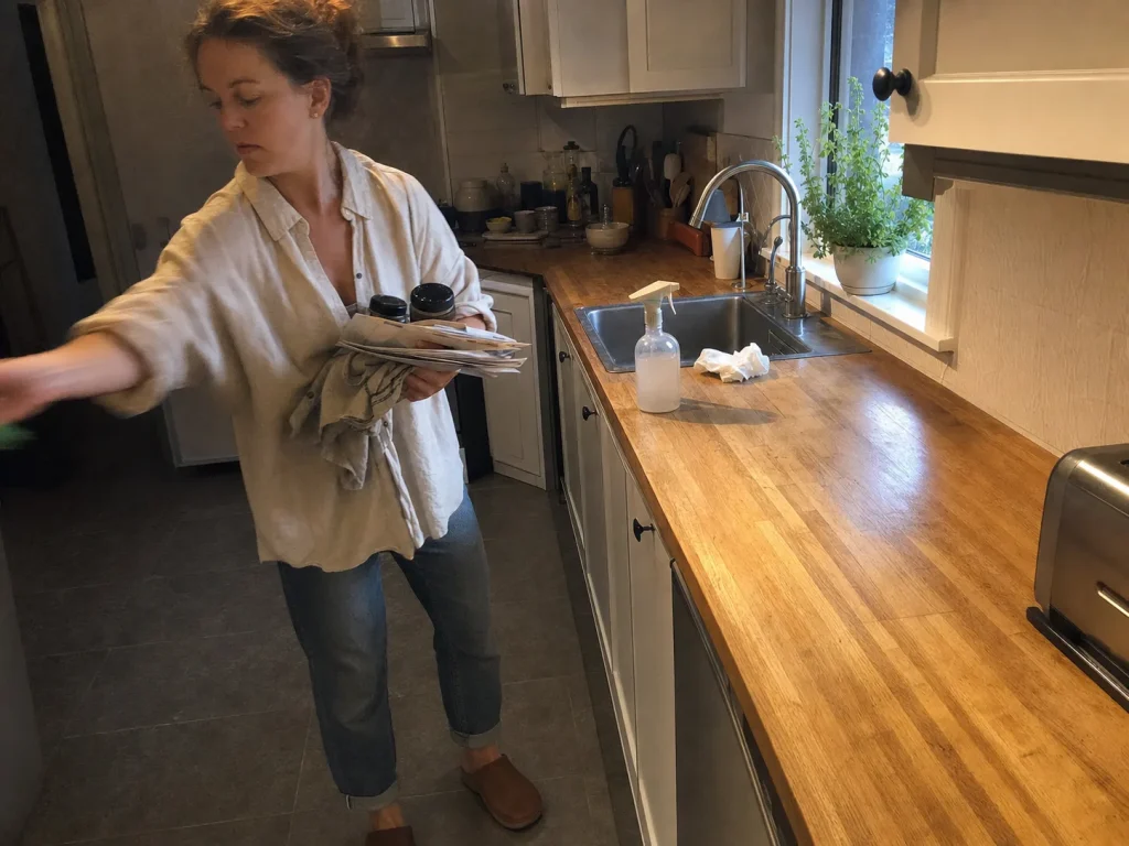 How to Declutter Kitchen Counters for Good 2 Woman clearing everything off a kitchen counter onto the table before sorting