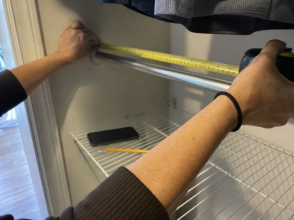 Hands measuring closet depth with a yellow tape measure before buying a rod extender