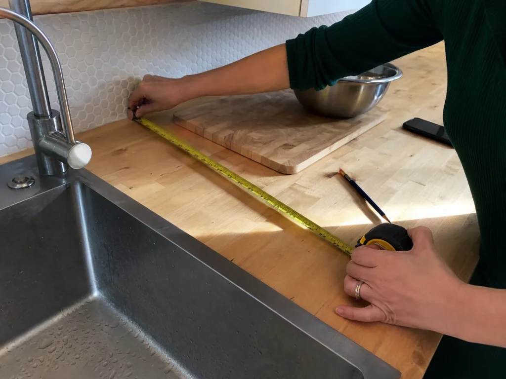 How to Organize Kitchen Counters That Stay Clear 2 Hands measuring the depth of a kitchen counter prep zone with a yellow tape measure