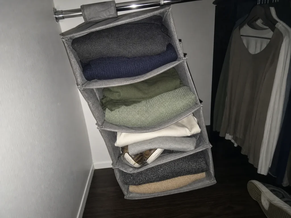 Close view of a sagging fabric hanging closet organizer with bowed middle shelves inside a dim closet