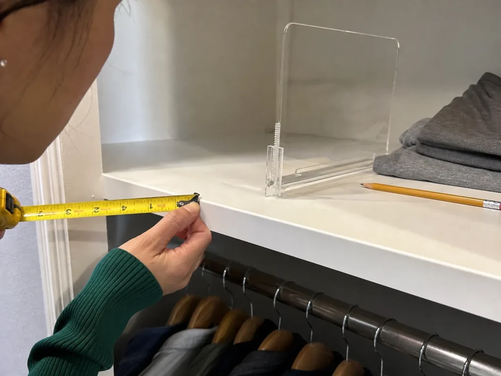 Hands measuring the thickness of a closet shelf's front edge next to an open clamp divider