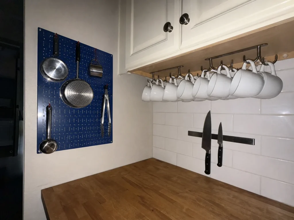 Wall pegboard and under-cabinet mug rack clearing a small kitchen counter with zero footprint