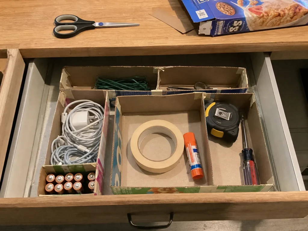 Junk drawer divided into categories using a grid built from cut cereal and tea boxes
