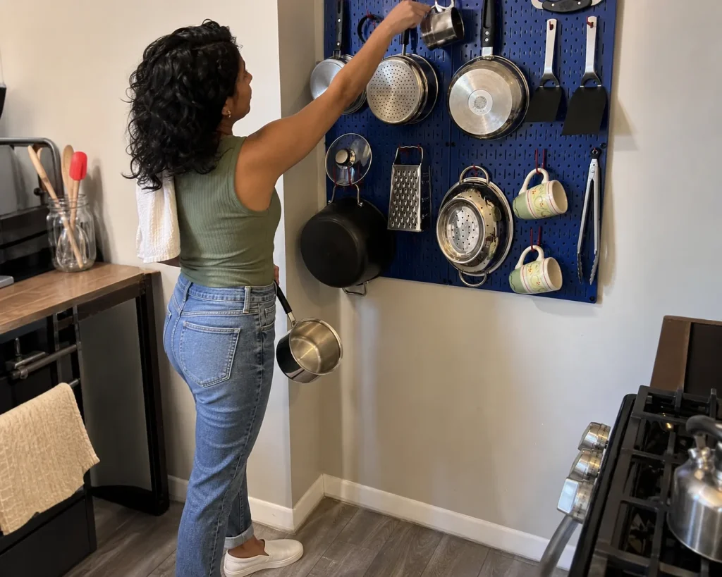 Woman hanging a pan on a kitchen pegboard to move storage up the wall in a small kitchen