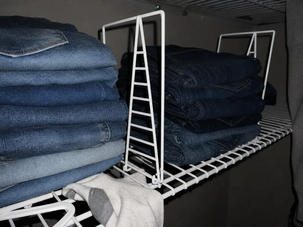 Coated-wire shelf divider being seated onto a deep wire shelf in a dim closet, lit by flash