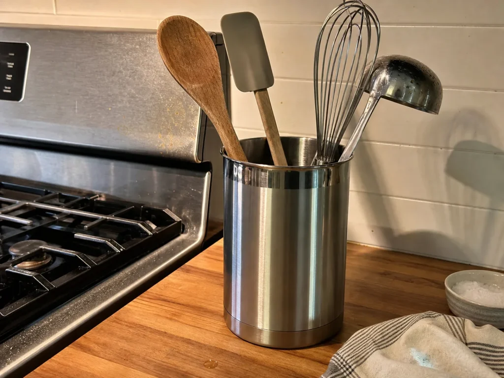 Stainless steel utensil crock holding cooking tools upright beside a kitchen stove