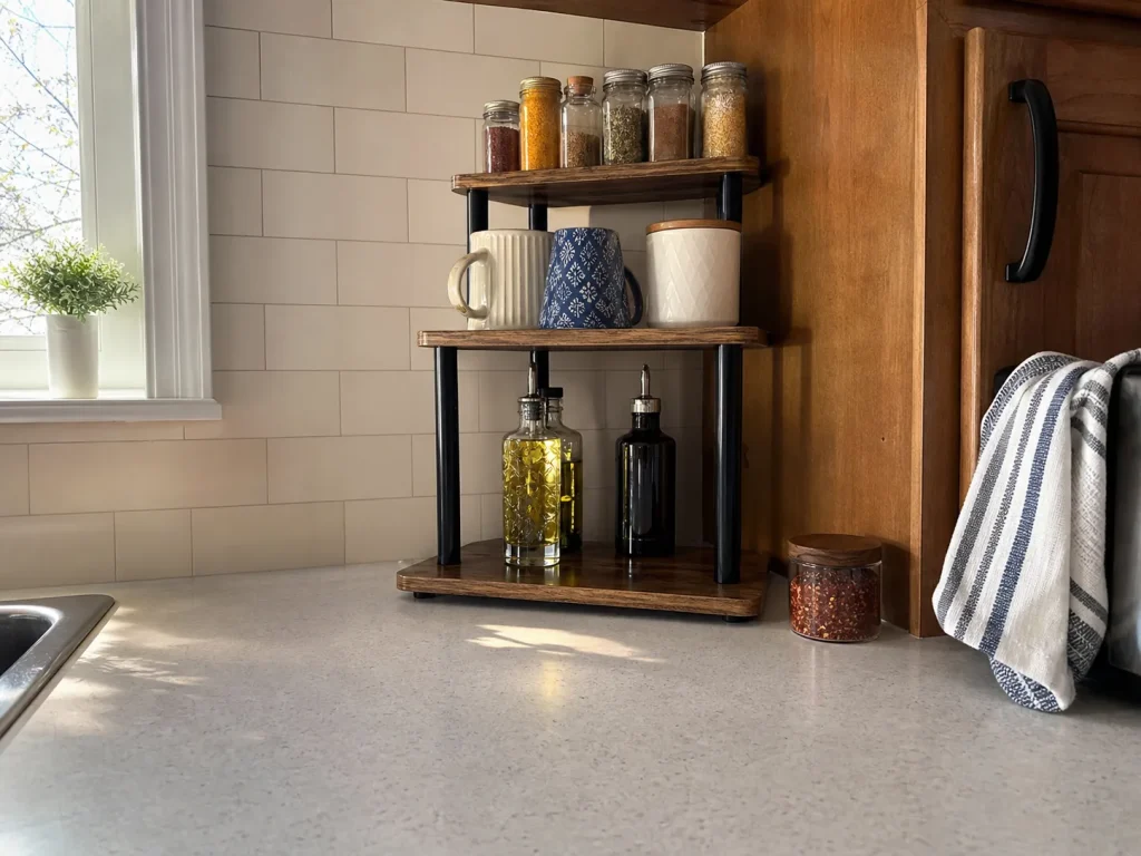Three-tier wood organizer stacking jars and mugs vertically against a kitchen backsplash