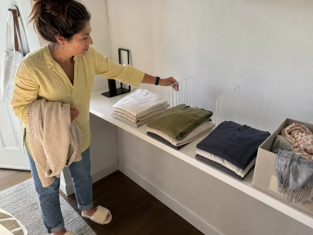 Woman spacing clear acrylic dividers between folded stacks beside a labeled fabric bin on a shelf