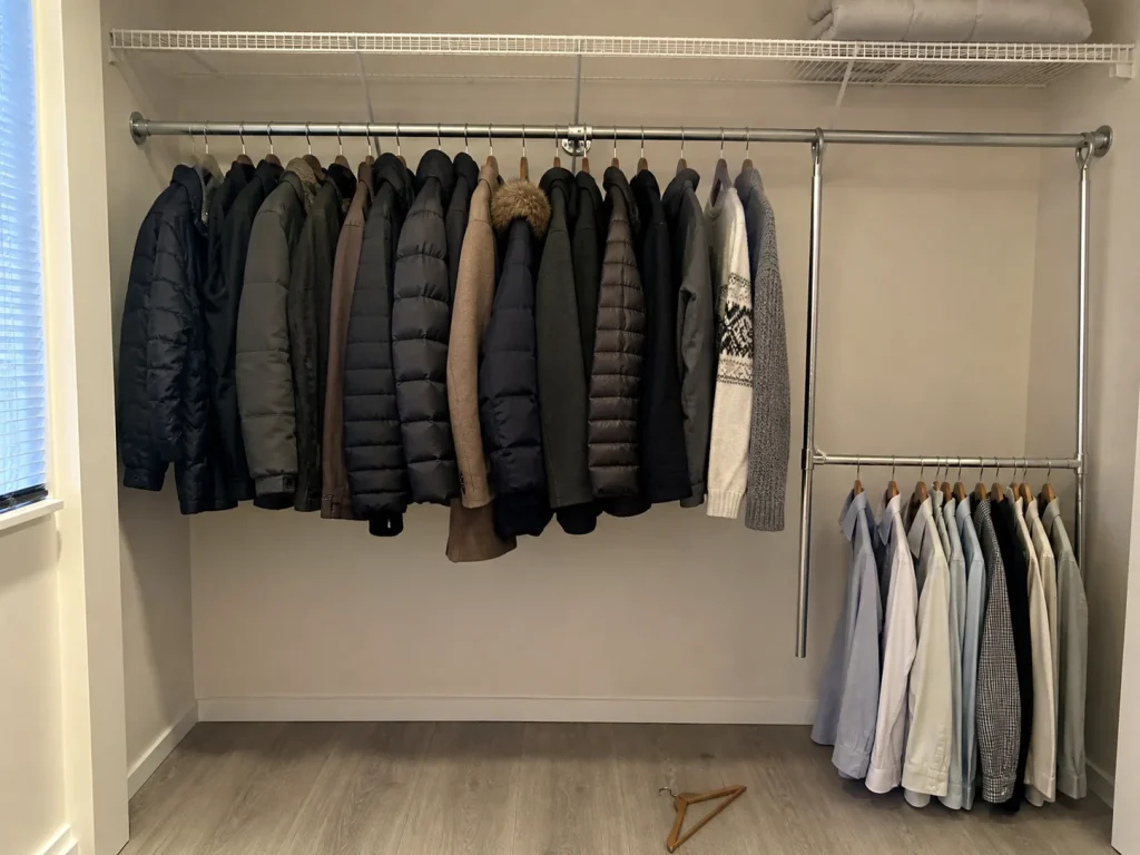 Rigid steel adjustable closet rod loaded with coats next to a lighter spring tension rod