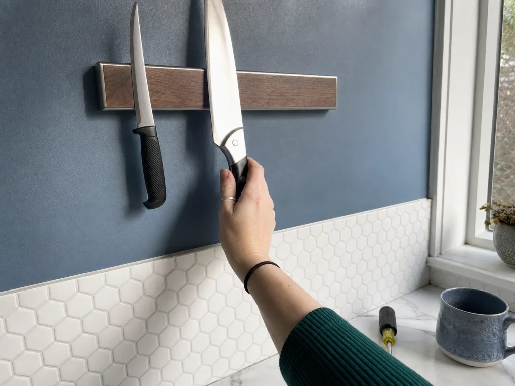 Hand placing a chef knife on a wall-mounted magnetic knife strip above a kitchen counter
