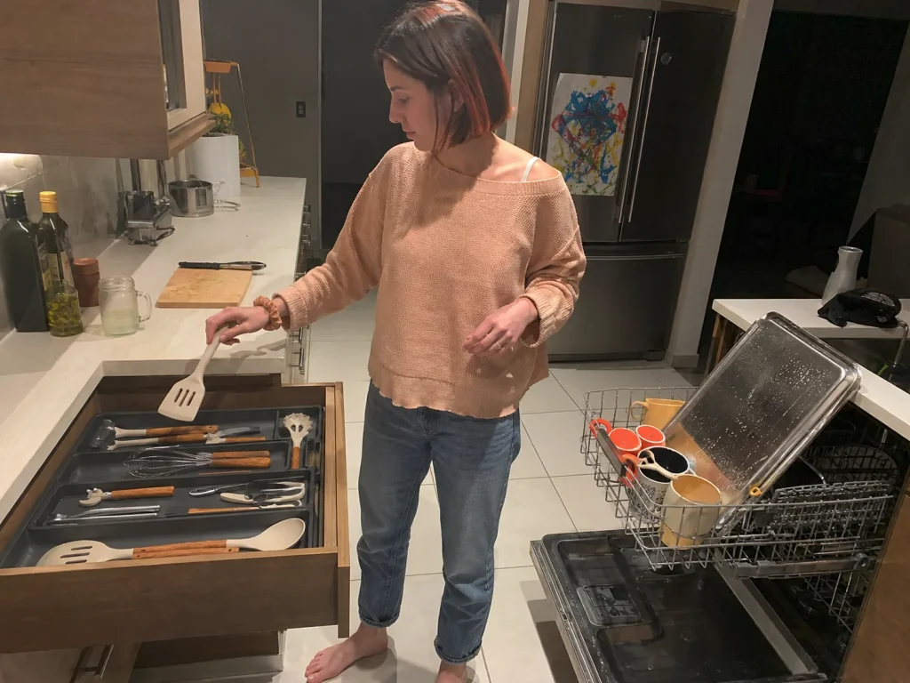 Woman putting a spatula back into a wide-zone plastic utensil drawer organizer after unloading the dishwasher