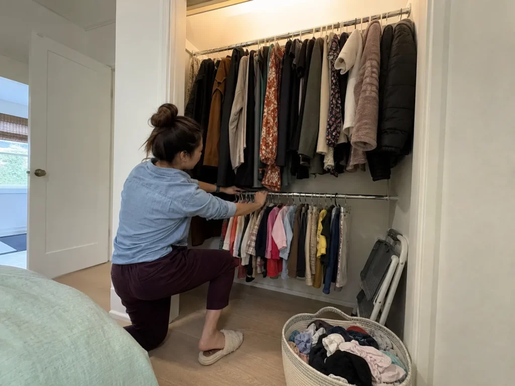 Woman setting a lower second rod in a shared closet so shorter clothes reach a lower tier
