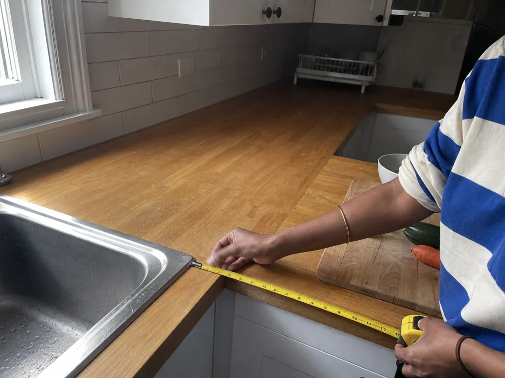 How to Declutter Kitchen Counters for Good 7 Hands measuring the clear prep-zone stretch of counter next to a kitchen sink with a tape measure