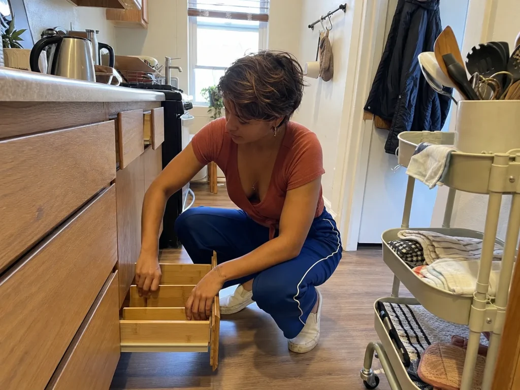 Woman in a small rental kitchen using a slim rolling cart and freestanding drawer dividers