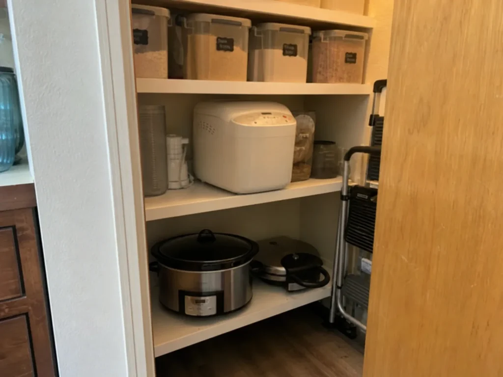 Pantry shelf storing rarely-used appliances like a waffle maker and slow cooker on a low shelf