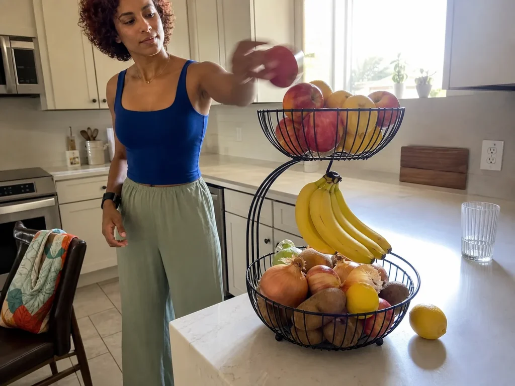 Woman placing an apple on a two-tier wire fruit basket on a kitchen counter to save space