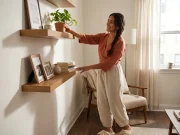 Best Floating Shelves for Small Spaces That Hold Up Woman placing a plant on a narrow wood floating shelf in a small organized living room