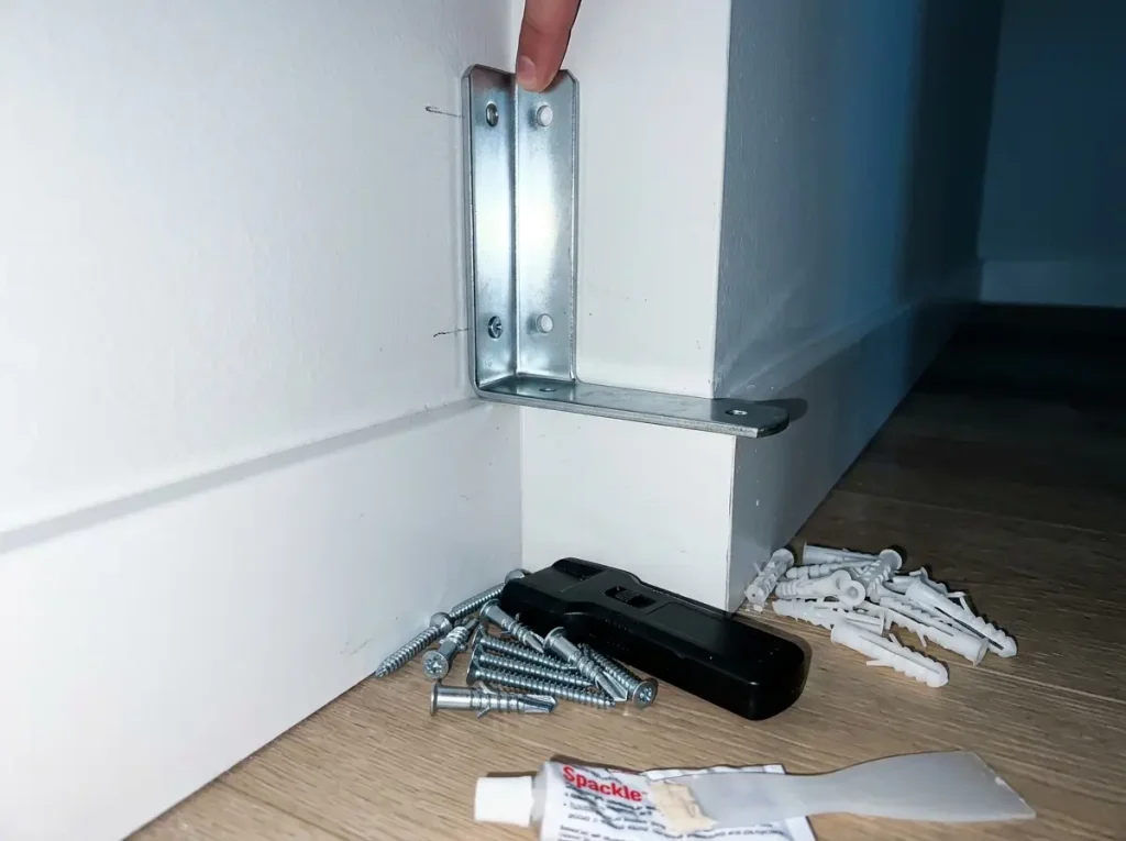 Metal L-bracket and wall anchors laid out for mounting a corner shelf into a stud