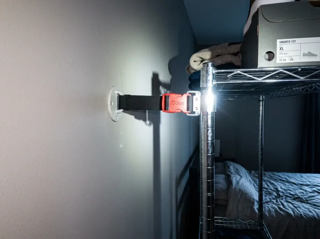 Anti-tip anchor strap connecting a tall freestanding shelf to a bedroom wall