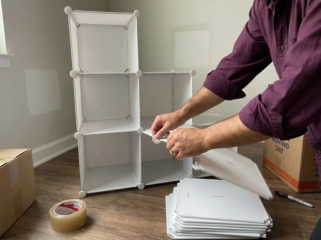 Hands disassembling a freestanding cube shelving unit into flat pieces during a move