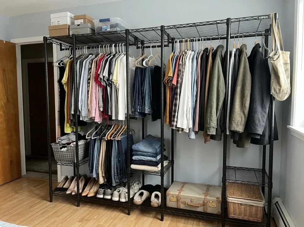 Freestanding steel closet system loaded with clothes in a rental bedroom, no wall attachment