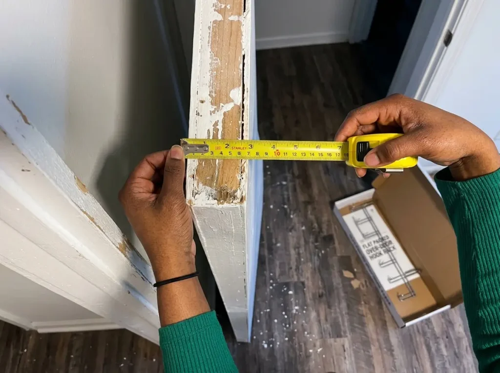 Hands measuring the thickness of a door's top edge with a yellow tape measure before buying an organizer