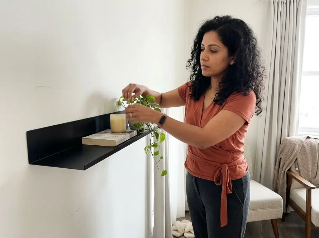 Renter placing a light plant on a no-stud black floating shelf in an apartment