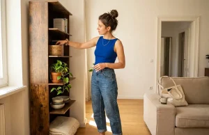 Shelving and Racks That Hold Up Where You Live Woman arranging a narrow freestanding shelf in a small apartment corner, shelving and racks that hold up