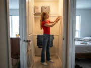 9 Tension Rod Shelving Ideas That Hold Real Weight Woman setting up tension rod shelving in a rental closet with folded stacks on the rods