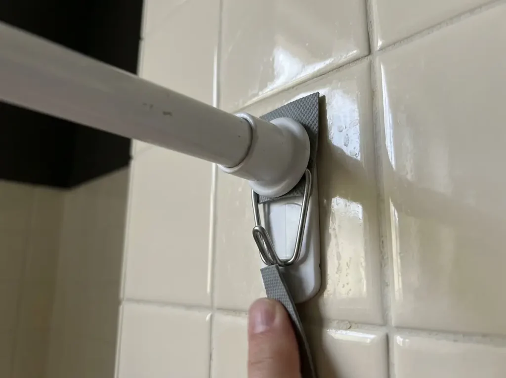 Close-up of a tension rod end cap on tile with a rubber liner strip and an adhesive wire hook below