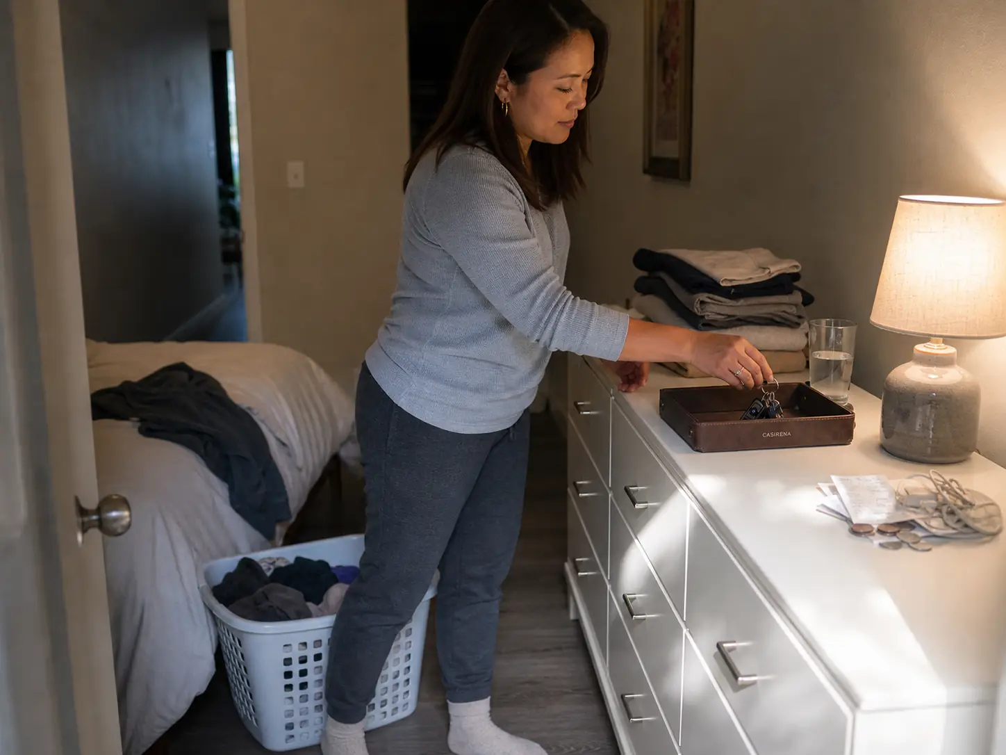 Dresser Top Organization Ideas That Survive Week Two Woman sorting a cluttered dresser top into a catch-all tray in a rental bedroom